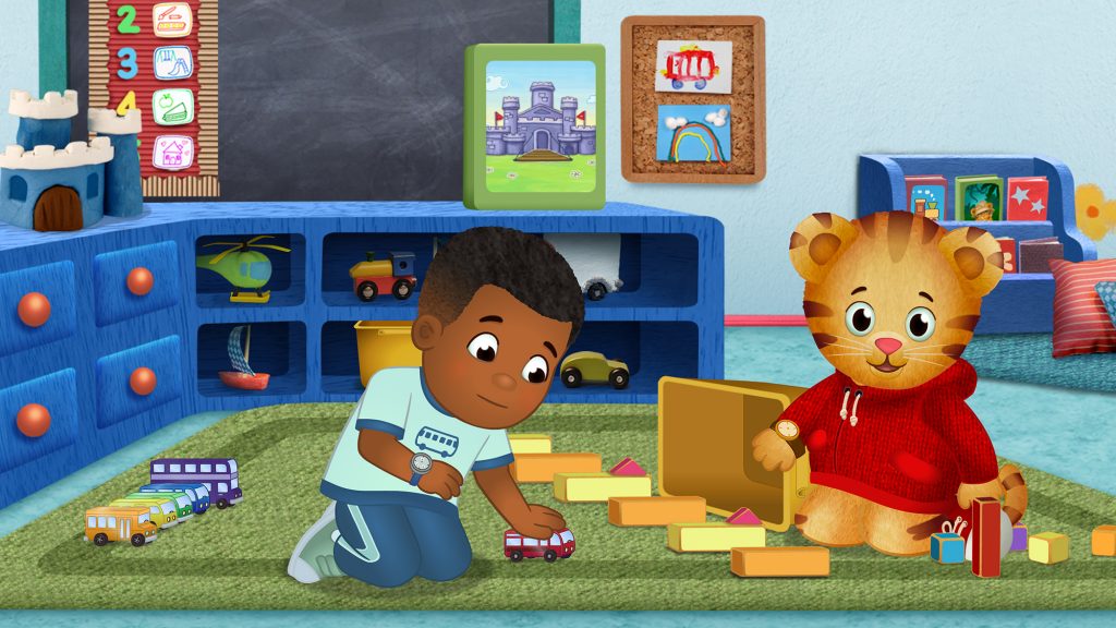 A boy places trucks with Daniel Tiger, the cartoon.