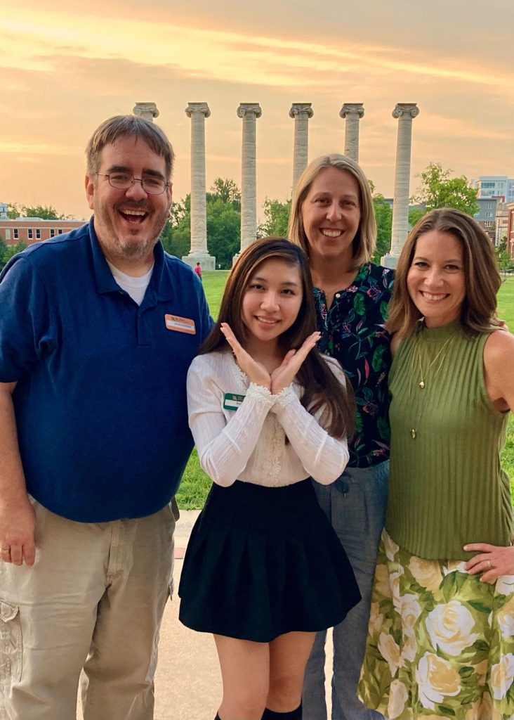 Four people smiling in front of historic columns on the University of Missouri - Columbia campus.